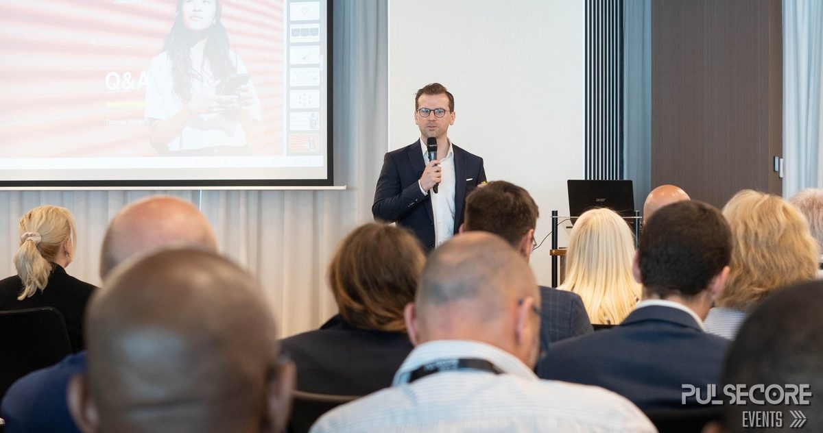 A speaker standing with a microphone addressing the room in front of a presentation screen